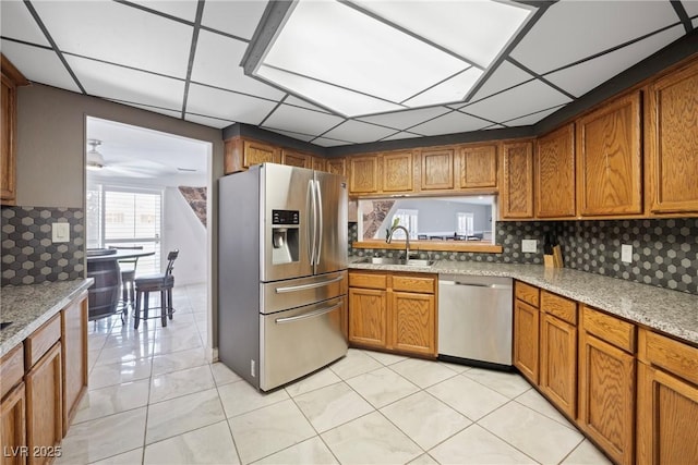 7215 Ullom Dr, Las Vegas, NV 89118 - kitchen with appliances with stainless steel finishes, tasteful backsplash, brown cabinetry, light tile patterned floors, and a drop ceiling