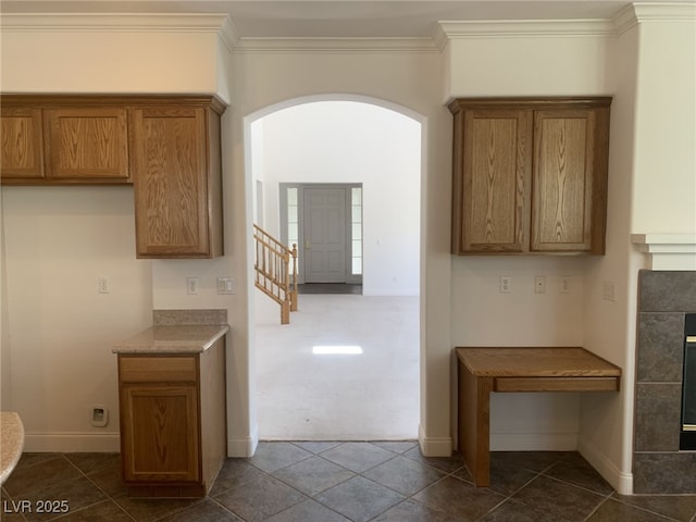 3328 White Bark Pine St, Las Vegas, NV 89129 - kitchen with arched walkways, brown cabinetry, crown molding, a tile fireplace, and dark tile patterned floors
