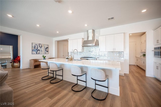11248 Rebel Dome Ct, Las Vegas, NV 89141 - kitchen featuring wall chimney exhaust hood, a breakfast bar, white cabinetry, light wood-style floors, and recessed lighting