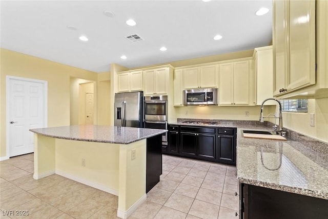 3012 Chiefs Ct, North Las Vegas, NV 89032 - kitchen featuring stainless steel appliances, a kitchen island, light stone counters, dark cabinetry, and light tile patterned floors