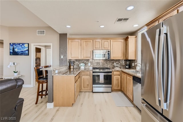 63 E Agate Ave Unit 509, Las Vegas, NV 89123 - kitchen with appliances with stainless steel finishes, light brown cabinets, a peninsula, light wood-type flooring, and a kitchen breakfast bar
