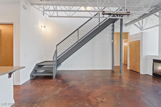 5603 Deer Creek Falls Ct, Las Vegas, NV 89118 - unfurnished living room with finished concrete floors, stairway, a glass covered fireplace, and a high ceiling