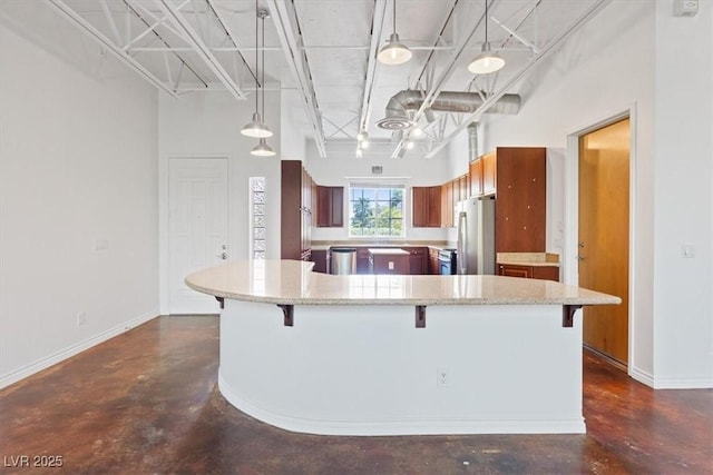 5603 Deer Creek Falls Ct, Las Vegas, NV 89118 - kitchen featuring stainless steel appliances, finished concrete floors, a breakfast bar, a high ceiling, and brown cabinets