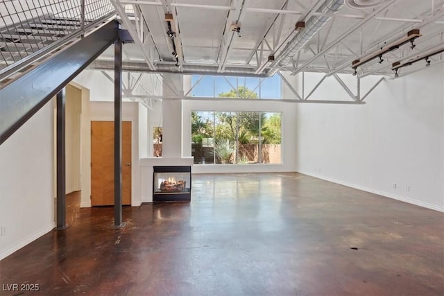 5603 Deer Creek Falls Ct, Las Vegas, NV 89118 - unfurnished living room featuring finished concrete flooring, a glass covered fireplace, and a high ceiling