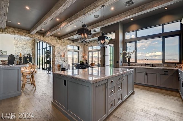 30 Via Tiberius Way, Henderson, NV 89011 - kitchen with gray cabinets, light wood-style floors, light stone counters, beam ceiling, and a kitchen island