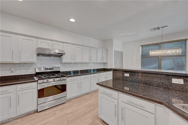 1069 Aspen Cliff Dr, Henderson, NV 89011 - kitchen featuring stainless steel gas range oven, under cabinet range hood, tasteful backsplash, dark stone counters, and pendant lighting