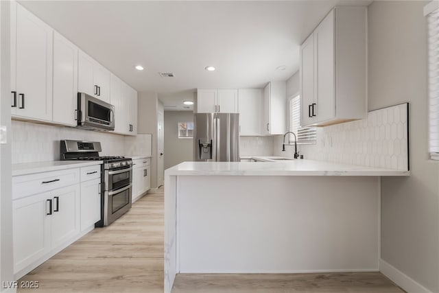 5417 Bible Cir, North Las Vegas, NV 89031 - kitchen featuring stainless steel appliances, light wood finished floors, backsplash, a peninsula, and white cabinets