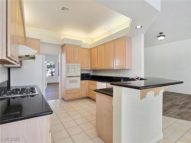 8981 Rivers Edge Dr, Las Vegas, NV 89117 - kitchen with light brown cabinets, white appliances, light tile patterned flooring, a peninsula, and a kitchen bar