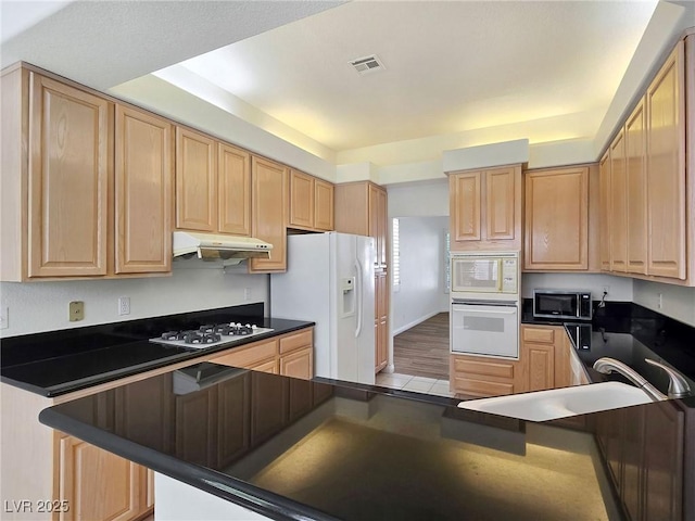 8981 Rivers Edge Dr, Las Vegas, NV 89117 - kitchen with white appliances, dark countertops, light brown cabinetry, and under cabinet range hood