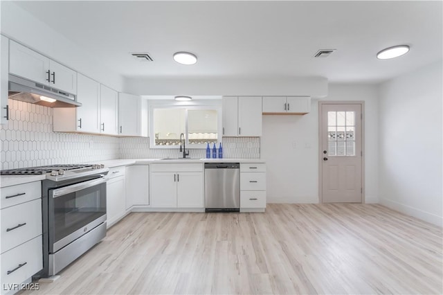 1808 E Saint Louis Ave, Las Vegas, NV 89104 - kitchen with stainless steel appliances, under cabinet range hood, tasteful backsplash, white cabinets, and light countertops