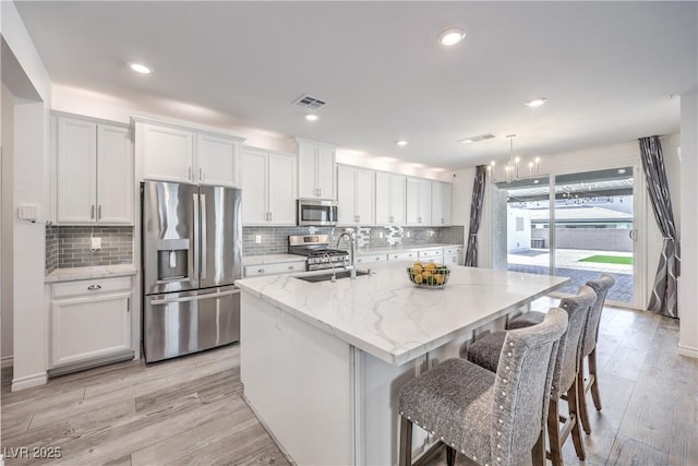 3821 Nesting Wren Dr, North Las Vegas, NV 89084 - kitchen with stainless steel appliances, white cabinetry, a center island with sink, decorative backsplash, and light wood-style flooring