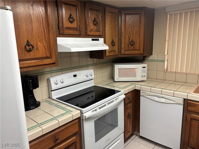4928 E Philadelphia Ave, Las Vegas, NV 89104 - kitchen featuring white appliances, under cabinet range hood, tile countertops, decorative backsplash, and light tile patterned floors