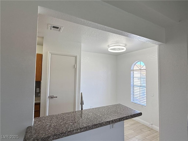 3606 Di Salvo Dr Unit 133, Las Vegas, NV 89103 - kitchen featuring dark countertops, a peninsula, light wood finished floors, a textured ceiling, and a kitchen breakfast bar