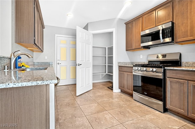 2175 Limestone Cove Ct, Laughlin, NV 89029 - kitchen featuring stainless steel appliances, light stone countertops, light tile patterned floors, and brown cabinetry