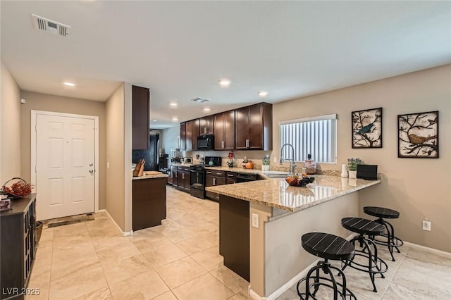 7224 Piute Mesa St, North Las Vegas, NV 89084 - kitchen with black appliances, a breakfast bar, light stone counters, a peninsula, and dark brown cabinetry