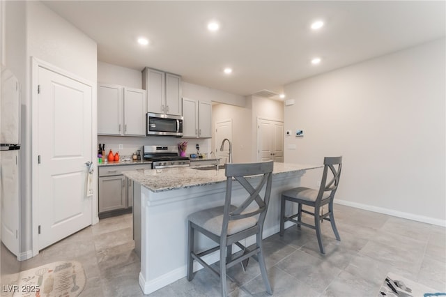 7910 Shimmery St, North Las Vegas, NV 89084 - kitchen featuring stainless steel appliances, a breakfast bar area, gray cabinetry, an island with sink, and recessed lighting
