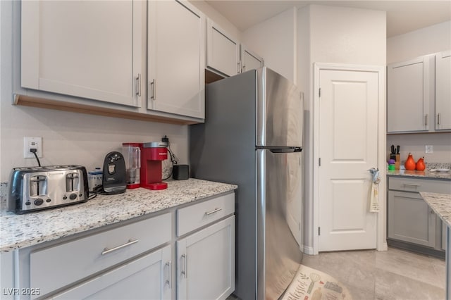 7910 Shimmery St, North Las Vegas, NV 89084 - kitchen with freestanding refrigerator, light stone countertops, gray cabinets, and light tile patterned floors