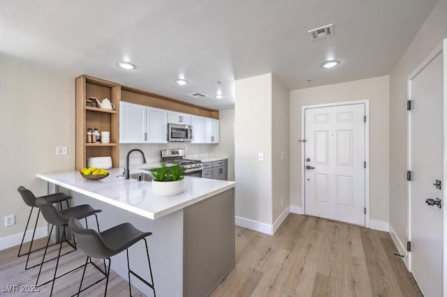 1097 Paradise Resort Dr, Henderson, NV 89002 - kitchen featuring appliances with stainless steel finishes, open shelves, a breakfast bar area, light countertops, and a peninsula