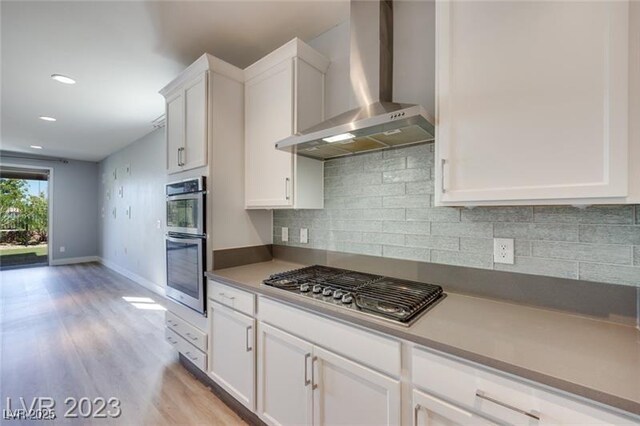10342 Kesington Dr, Las Vegas, NV 89135 - kitchen featuring wall chimney range hood, appliances with stainless steel finishes, light wood-type flooring, white cabinetry, and recessed lighting