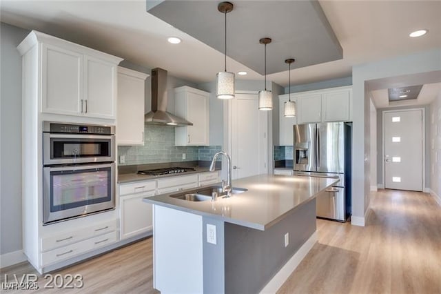 10342 Kesington Dr, Las Vegas, NV 89135 - kitchen with appliances with stainless steel finishes, wall chimney range hood, an island with sink, tasteful backsplash, and light wood finished floors