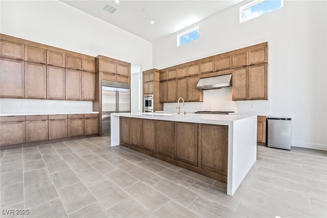 10919 Vista Altura Ave, Las Vegas, NV 89135 - kitchen with a high ceiling, appliances with stainless steel finishes, under cabinet range hood, light countertops, and brown cabinets