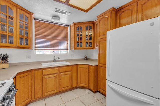 825 W Ryan Ave, Overton, NV 89040 - kitchen with freestanding refrigerator, range with gas stovetop, light tile patterned flooring, brown cabinets, and glass insert cabinets