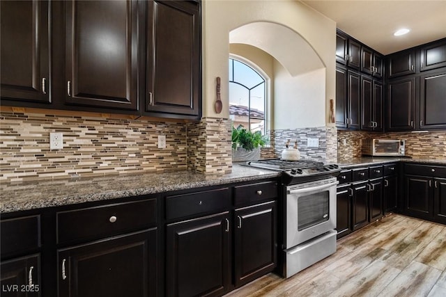 6705 Philharmonic Ave, Las Vegas, NV 89139 - kitchen with stainless steel range with gas cooktop, light wood-style flooring, tasteful backsplash, dark stone countertops, and arched walkways