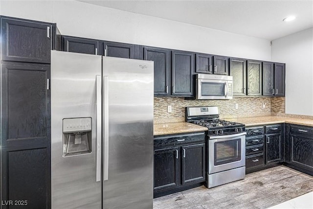 3257 Rushing Waters Pl, Las Vegas, NV 89135 - kitchen featuring appliances with stainless steel finishes, tasteful backsplash, dark cabinetry, and light wood-style floors