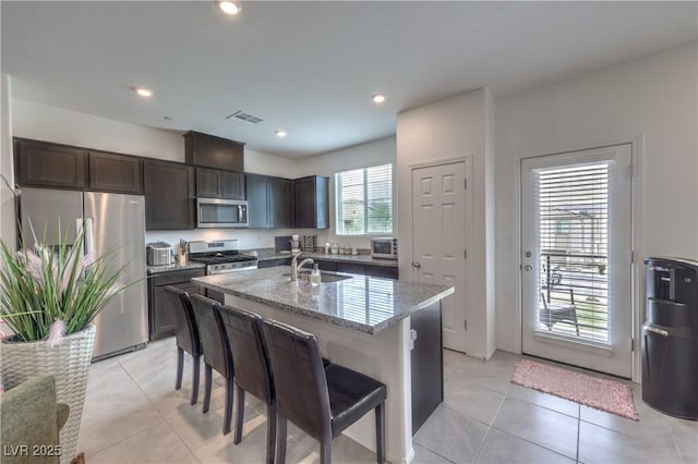 1120 Tektite Ave, Henderson, NV 89011 - kitchen with stainless steel appliances, light stone counters, dark brown cabinets, a kitchen breakfast bar, and a center island with sink