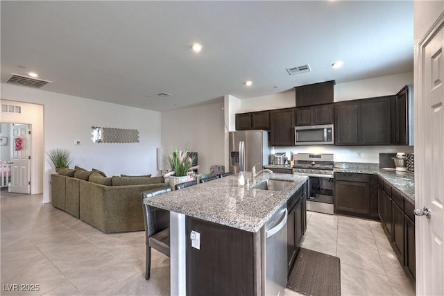 1120 Tektite Ave, Henderson, NV 89011 - kitchen featuring stainless steel appliances, open floor plan, light tile patterned flooring, light stone counters, and dark brown cabinetry