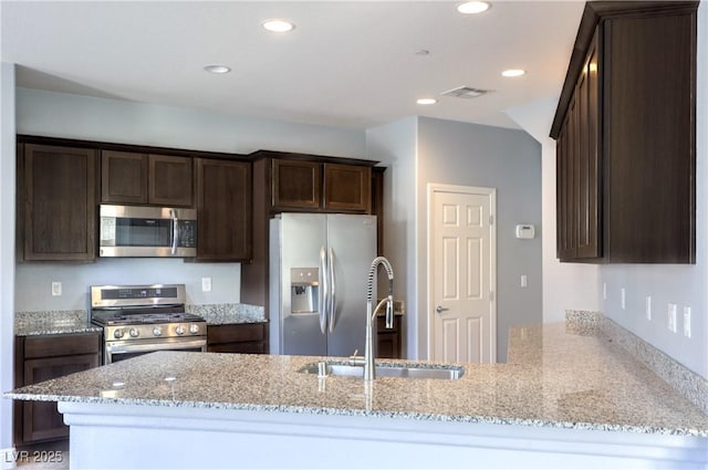 2300 Sky Island Dr, Henderson, NV 89002 - kitchen with appliances with stainless steel finishes, dark brown cabinets, light stone countertops, a peninsula, and recessed lighting