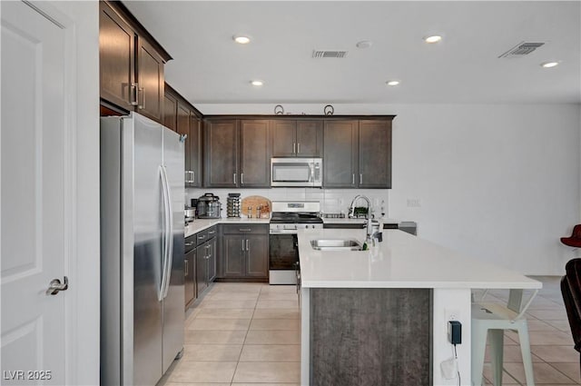 7853 Bethel Heights Ln, Las Vegas, NV 89113 - kitchen featuring stainless steel appliances, light tile patterned floors, dark brown cabinetry, a kitchen island with sink, and tasteful backsplash