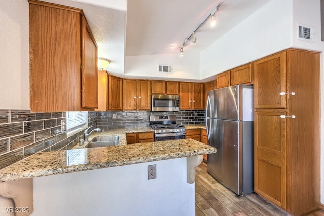 520 Arrowhead Trl Unit 522, Henderson, NV 89015 - kitchen with stainless steel appliances, a peninsula, light stone counters, brown cabinets, and light wood-style flooring