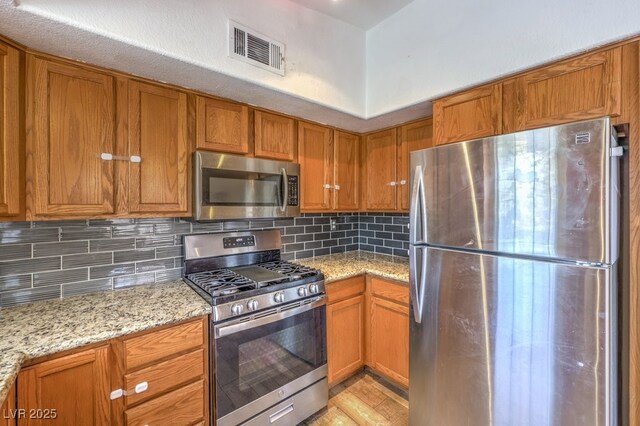 520 Arrowhead Trl Unit 522, Henderson, NV 89015 - kitchen with appliances with stainless steel finishes, brown cabinets, tasteful backsplash, and light stone counters