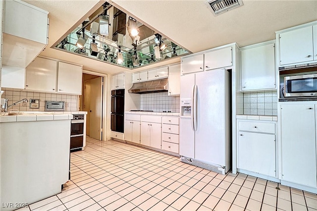 940 Vegas Valley Dr, Las Vegas, NV 89109 - kitchen featuring white refrigerator with ice dispenser, tile countertops, stainless steel microwave, under cabinet range hood, and decorative backsplash