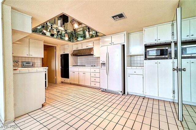 940 Vegas Valley Dr, Las Vegas, NV 89109 - kitchen with white refrigerator with ice dispenser, stainless steel microwave, decorative backsplash, tile countertops, and under cabinet range hood