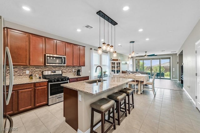 2383 Elmont Ave, North Las Vegas, NV 89086 - kitchen with appliances with stainless steel finishes, light stone counters, decorative backsplash, brown cabinetry, and ceiling fan