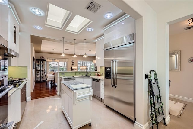 1897 Holdenville St, Henderson, NV 89052 - kitchen featuring appliances with stainless steel finishes, a peninsula, white cabinetry, pendant lighting, and a kitchen island