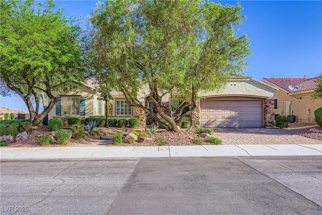 1897 Holdenville St, Henderson, NV 89052 - view of property hidden behind natural elements featuring decorative driveway, stone siding, an attached garage, and stucco siding