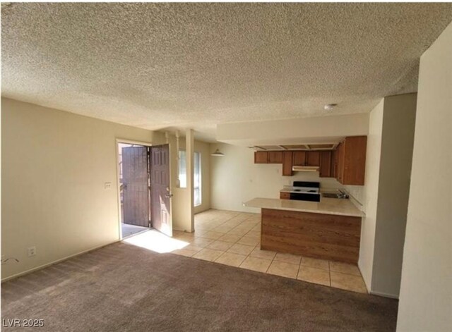 4300 N Lamont St Unit 232, Las Vegas, NV 89115 - kitchen with range, brown cabinets, under cabinet range hood, a peninsula, and light colored carpet