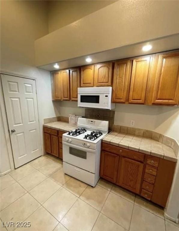 3237 Perching Bird Ln, North Las Vegas, NV 89084 - kitchen featuring white appliances, brown cabinets, light tile patterned floors, tile countertops, and a high ceiling