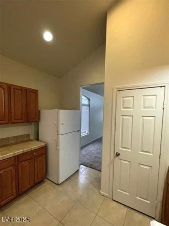 3237 Perching Bird Ln, North Las Vegas, NV 89084 - kitchen with freestanding refrigerator, tile countertops, vaulted ceiling, brown cabinetry, and light tile patterned flooring