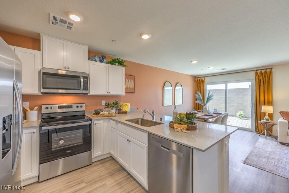 10982 Rollingford Ave Lot 7, Las Vegas, NV 89166 - kitchen featuring stainless steel appliances, a peninsula, light wood-type flooring, open floor plan, and white cabinetry