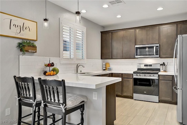 1113 Fragrant Cactus Ct, North Las Vegas, NV 89031 - kitchen featuring appliances with stainless steel finishes, dark brown cabinets, a peninsula, tasteful backsplash, and recessed lighting
