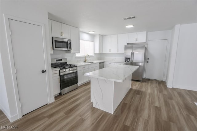 4269 Roanridge Ave, Las Vegas, NV 89120 - kitchen with stainless steel appliances, light wood finished floors, a kitchen island, light stone counters, and white cabinetry