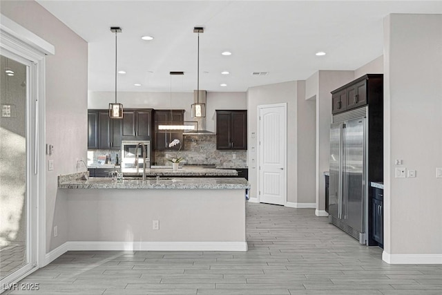 274 Chartan Ave, Las Vegas, NV 89183 - kitchen featuring stainless steel appliances, wall chimney range hood, dark brown cabinetry, wood tiled floors, and a peninsula