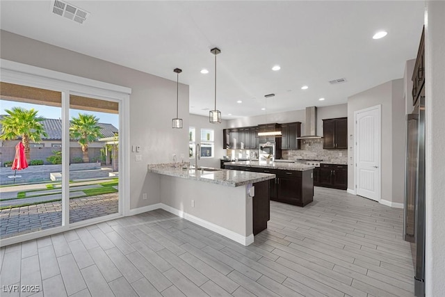 274 Chartan Ave, Las Vegas, NV 89183 - kitchen with wall chimney range hood, dark brown cabinets, a kitchen island, decorative backsplash, and a peninsula