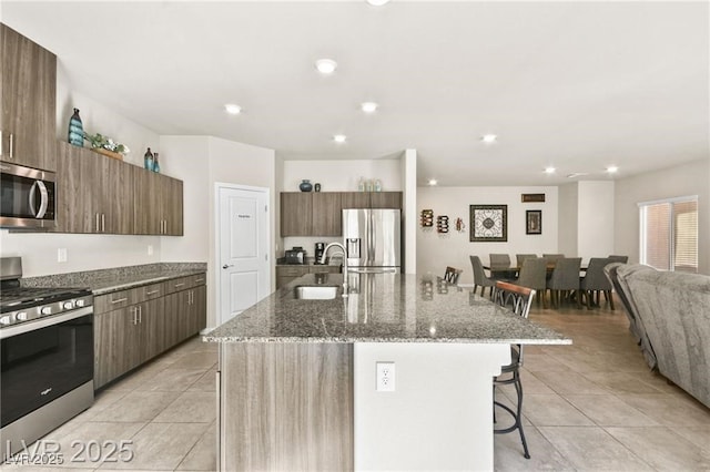 8937 Pelican Point St, Las Vegas, NV 89178 - kitchen featuring stainless steel appliances, a breakfast bar area, light tile patterned flooring, stone countertops, and a kitchen island with sink