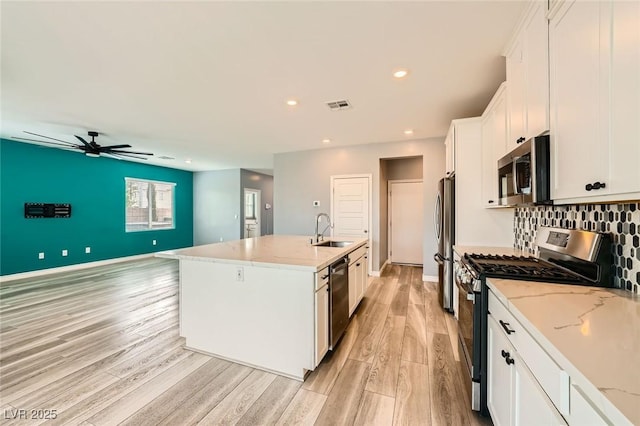 5990 Viscaya Grove St, Las Vegas, NV 89118 - kitchen featuring appliances with stainless steel finishes, white cabinetry, light wood finished floors, a center island with sink, and light stone counters