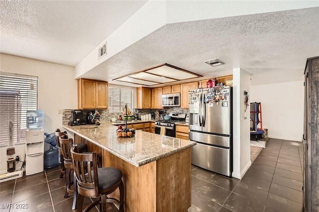 5754 Cinnabar Ave, Las Vegas, NV 89110 - kitchen featuring stainless steel appliances, a peninsula, a textured ceiling, dark tile patterned flooring, and a breakfast bar area
